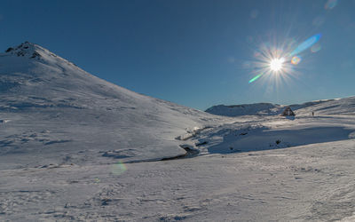 Panoramic view of chalet house in snow covered mountains with sun and camera flare on a clear day