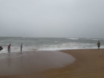 People standing on beach against clear sky