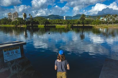 Rear view of woman standing by lake against sky