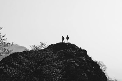 Low angle view of people walking on mountain against clear sky