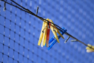 Low angle view of clothespins hanging by fence against sky