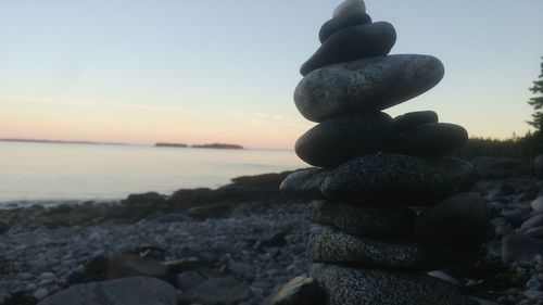 Stack of stones on beach against sky during sunset