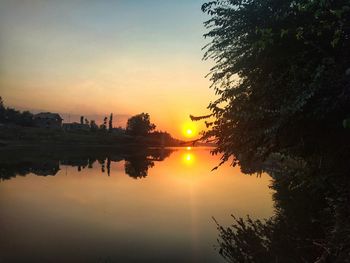 Silhouette trees by lake against sky during sunset