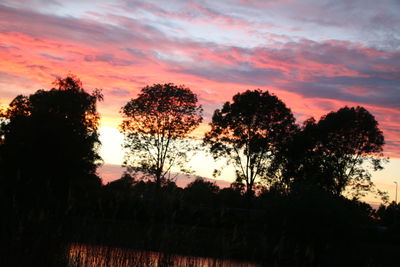 Silhouette trees on field against romantic sky at sunset