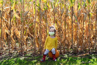 Portrait of cute girl wearing mask sitting on pumpkin at farm