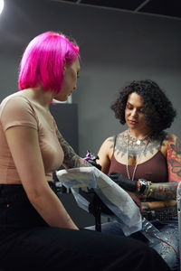 Tattoo master in gloves using professional tattoo machine while painting tattoo on arm of woman in modern tattoo studio