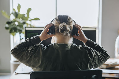 Rear view of female programmer wearing headphones while sitting in tech startup office