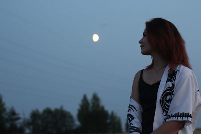 Young woman looking away against sky at dusk