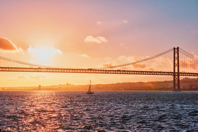 Suspension bridge over river against sky during sunset