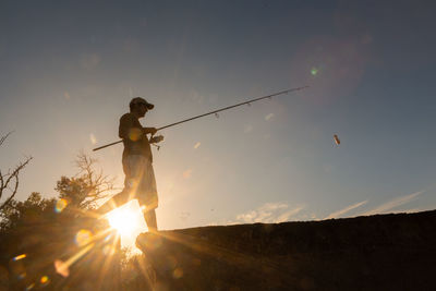 Low angle view of man holding fishing rod walking on pie by lake