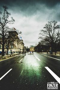 Road by trees in city against sky