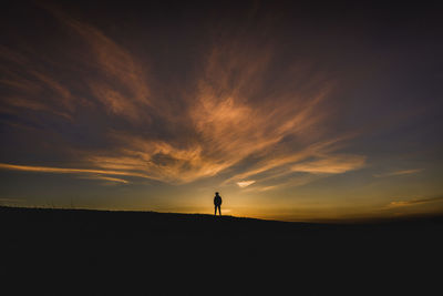 Silhouette person standing on field against sky during sunset