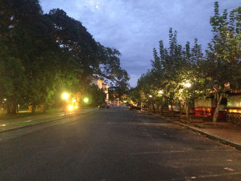 Empty road along trees and buildings at dusk