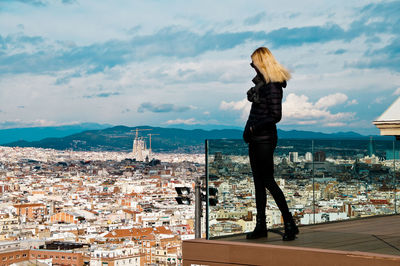 Young woman wearing warm clothing while standing on balcony against cityscape