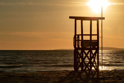 Lifeguard hut on beach against sky during sunset