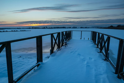 Snow on the pier and a frozen lake, clouds on the sky after sunset, winter landscape