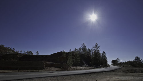 Road amidst trees against clear blue sky