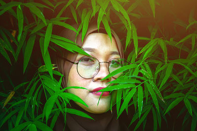 Close-up portrait of woman with eyeglasses amidst plant