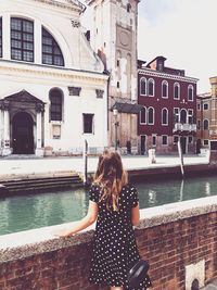 Rear view of woman standing by canal in city