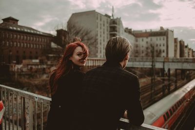 Rear view of friends standing against railing in city