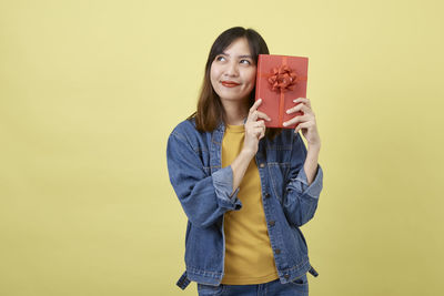 Portrait of young woman standing against yellow background