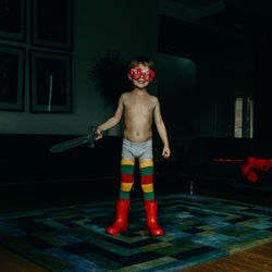 Full length portrait of shirtless boy standing against wall at night