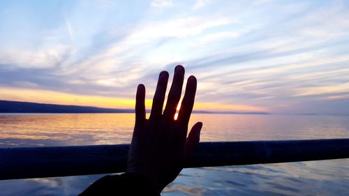 Close-up of hand against sea during sunset