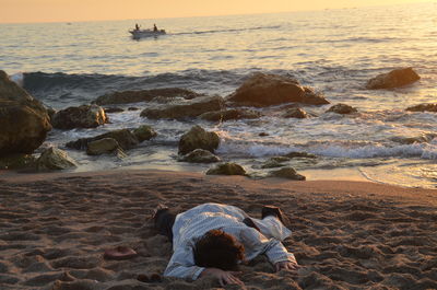 Man lying at beach against sky