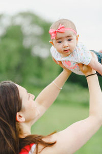 Young adult woman looking up and holding baby girl above head with child looking at camera