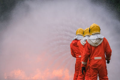 Rear view of firefighters spraying water on fire while standing on land