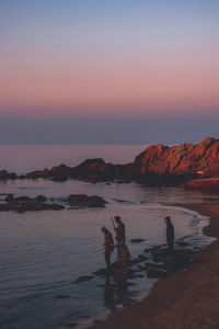 People on beach against sky during sunset