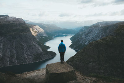 Rear view of man standing on cliff with valley in background against sky