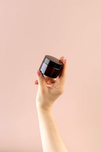 Mockup of a glass brown jar with a cosmetic product in a female hand on a light pink background. 