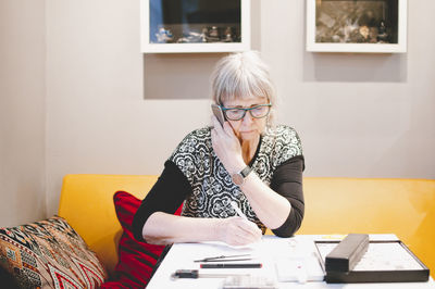 Senior woman talking on mobile phone while sitting at desk in jewelry workshop