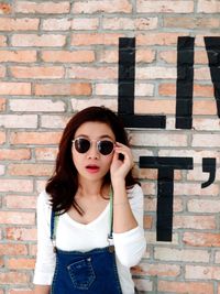 Portrait of young woman wearing sunglasses standing against brick wall