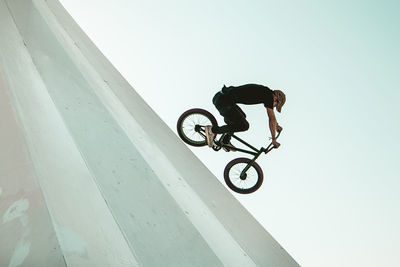 Man riding bicycle on built structure against sky