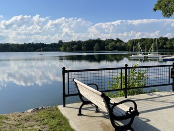 Bench by lake against sky