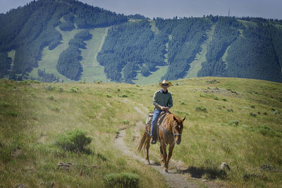 Cowboy riding horse on field against mountain