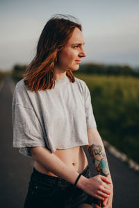 Side view of young woman standing against sky