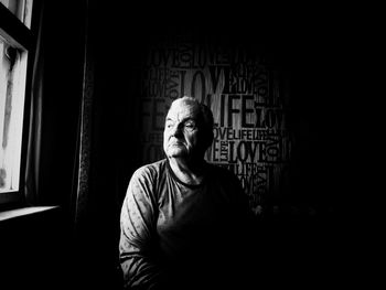 Thoughtful senior man against wall with text in darkroom