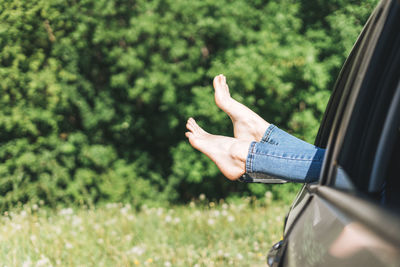 Slim woman legs barefoot in jeans in car window on the background of summer meadow, summertime 