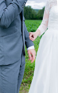 Midsection of bride and groom standing on field