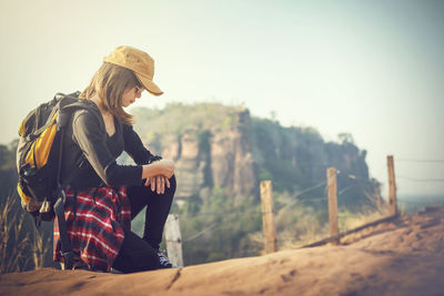 Young woman sitting on land against sky