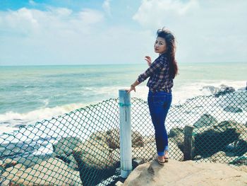 Portrait of young woman standing by sea against sky