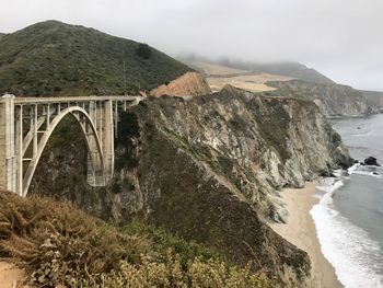 Arch bridge over sea by mountains against sky