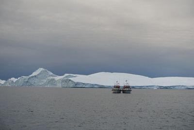 Boats on sea against icebergs