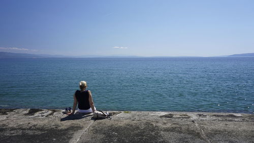 Rear view of man sitting on beach against clear sky