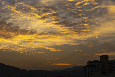 Silhouette buildings against dramatic sky during sunset