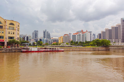 Buildings by river against cloudy sky