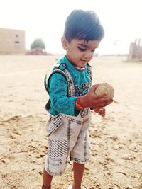 Cute boy holding stone while standing at beach
